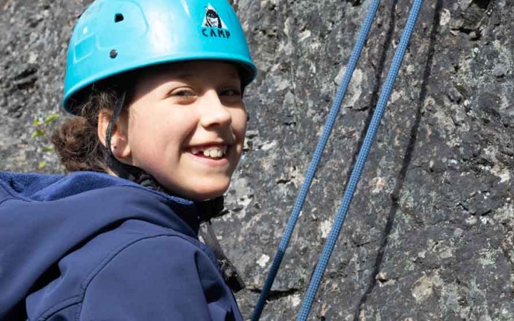 a girl smiles at the camera while rock climbing with outward bound